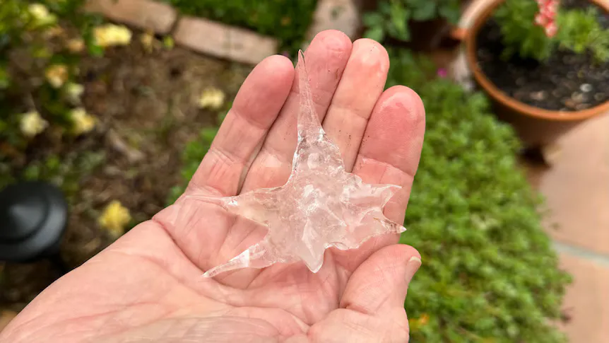 Hailstones scattered across grass beneath a dark storm sky