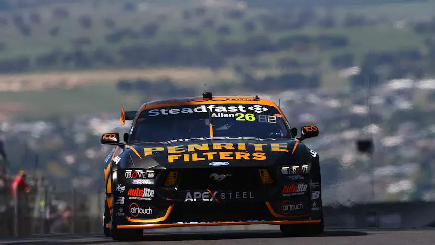 Racing cars on a circuit with pit garages in the background